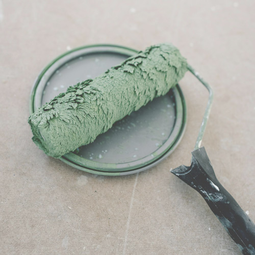 rouleau de peinture avec de la peinture verte posé par terre
